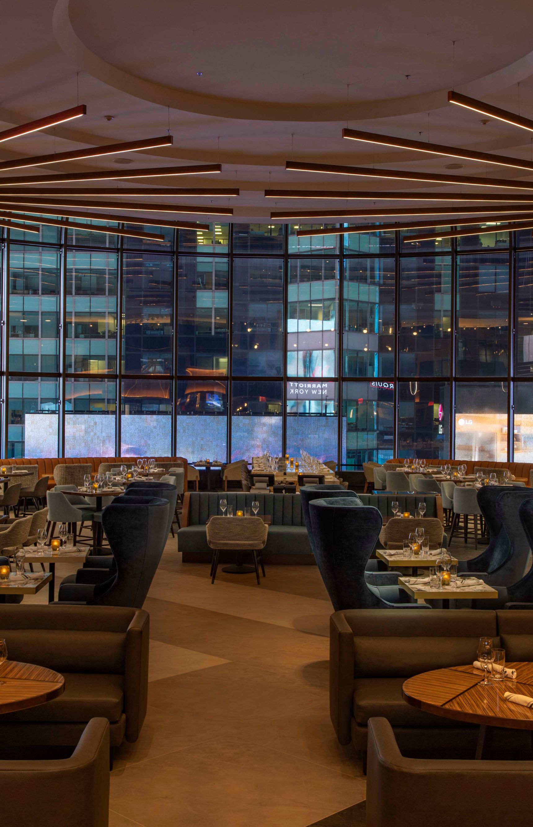 A large lounge with various seats, booths and tables with a wall of windows in the back.