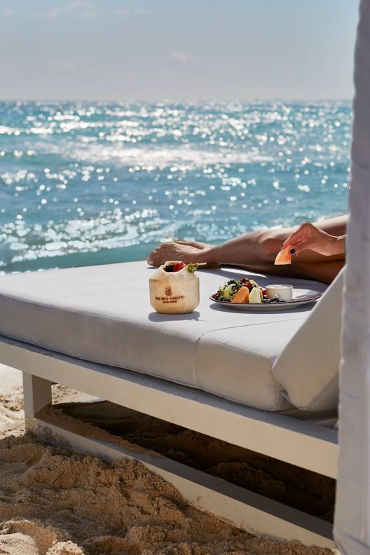 Beach chair with a plate of food on top and the ocean in the background.