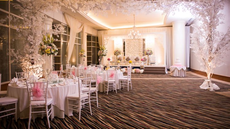 Event space featuring white faux tree branches arching over white tables accented with pink