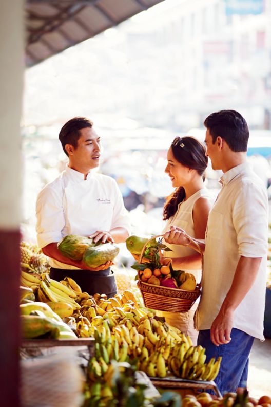 Couple fills their baskets with fruit and vegetables at a street stall while a chef explains the finer points of food shopping