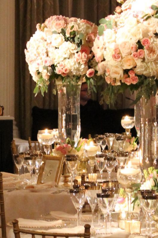 Large floral decorations, candles and silverware on a table with the open bar behind it.