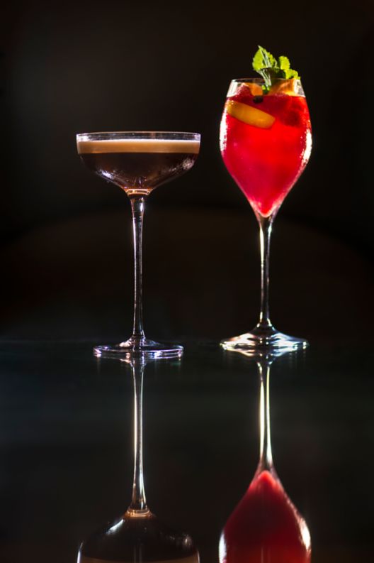 A chocolatey brown cocktail and a strawberry red cocktail placed side-by-side against a black background