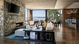A lounge area with a fire place, bar and floor-to-ceiling windows overlooking a lake