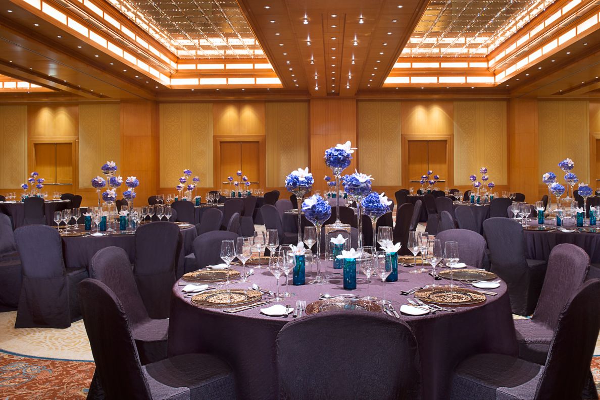 Roundtables and chairs all draped in deep violet cloth with centerpieces of blue and white florals