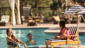 A young girl sits near the pool as her parents splash her with water