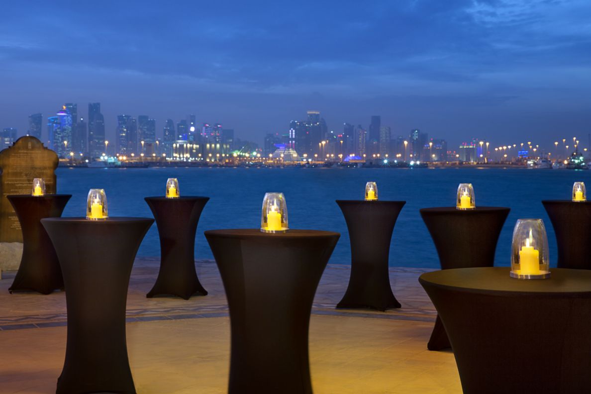 High-top tables with lights on the table top placed on the beach facing the sea.
