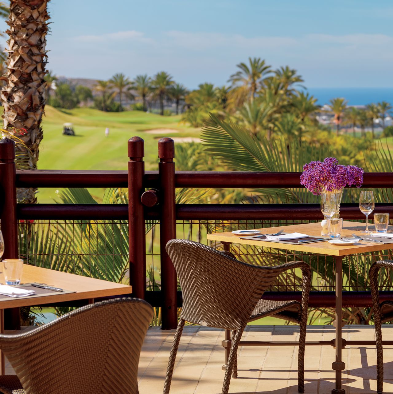 Dining tables on a patio overlooking a golf course and the ocean