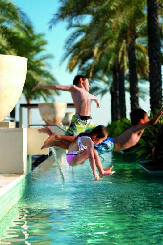 Three children jumping into the emerald green waters of the hotel pool.