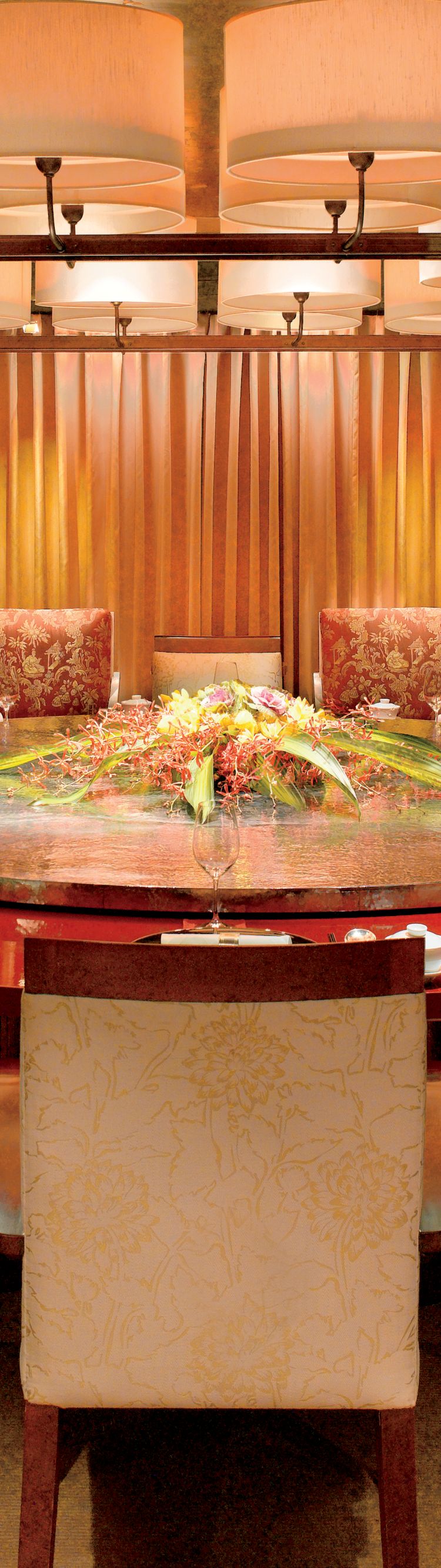 Roundtable in a private dining space with dark wood paneling on the sides, curtains at the back and a lamp-like light fixture