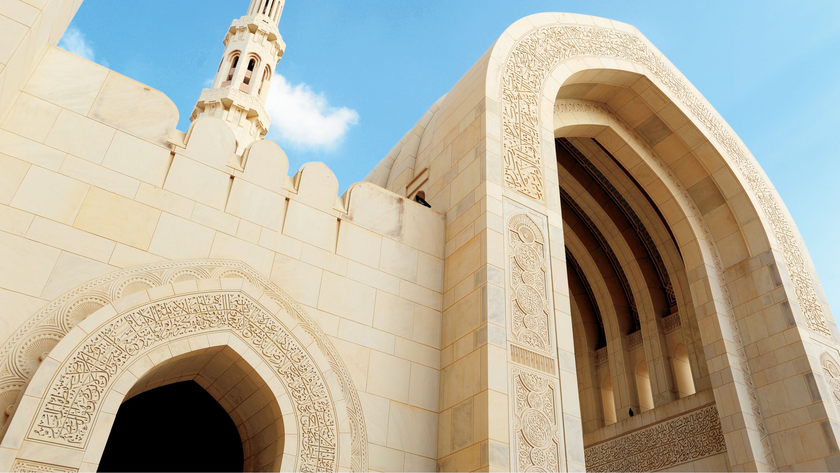 Upward view of a grand mosque built in white stone with a minaret and blue skies in the background