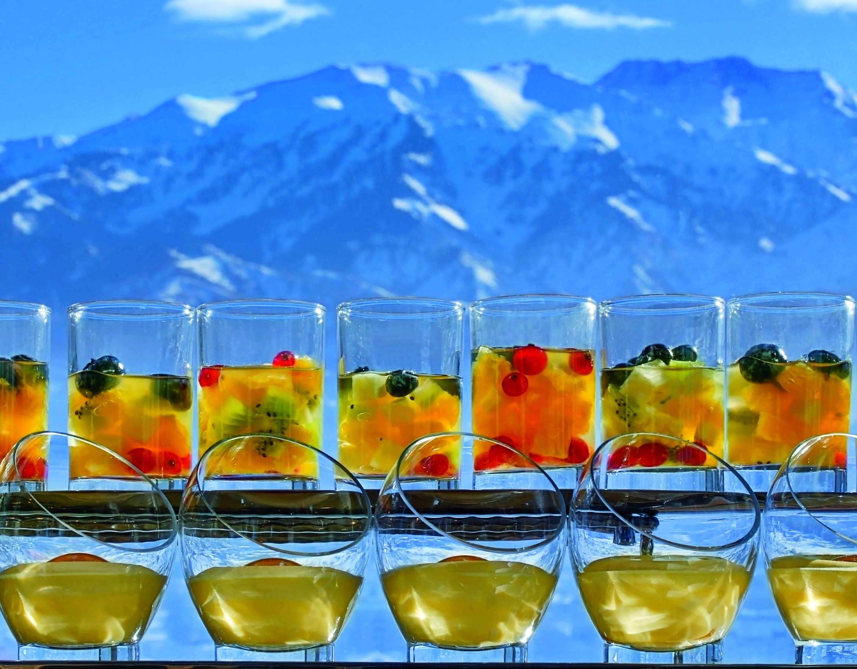 A row of glasses, filled with fruit cocktails and custard, overlooking snow-capped mountains