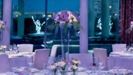 Dining tables with formal place settings and tall floral centerpieces surrounded by smaller flower vases