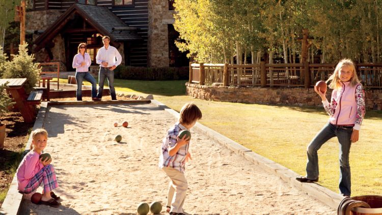 A family of five plays on an outdoor bocce ball court