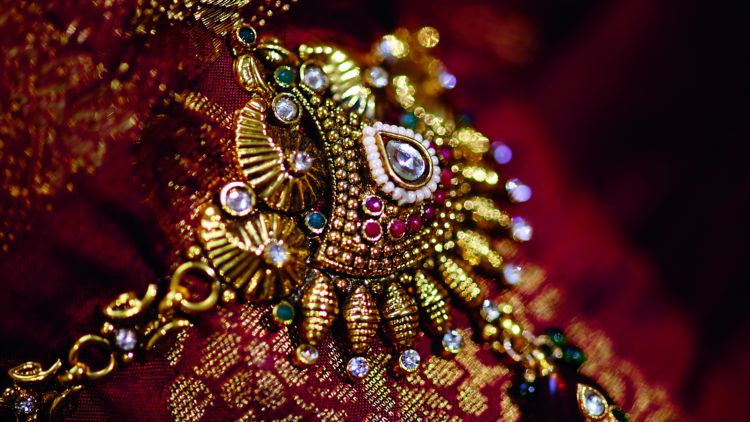 An ornate piece of Indian jewelry against a colorful Indian fabric