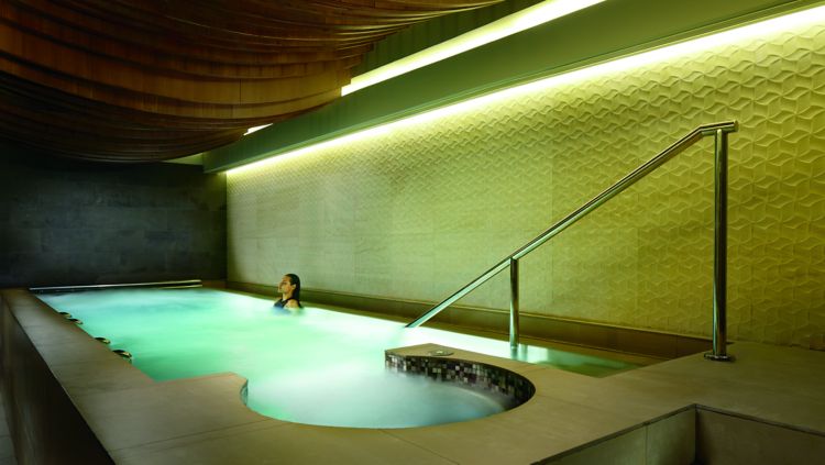 A woman relaxing in a large rectangular whirlpool beneath a ceiling of curved wood
