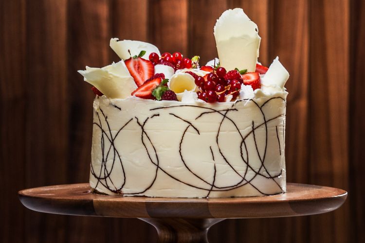 A white chocolate cake topped with fruit on a wood stand