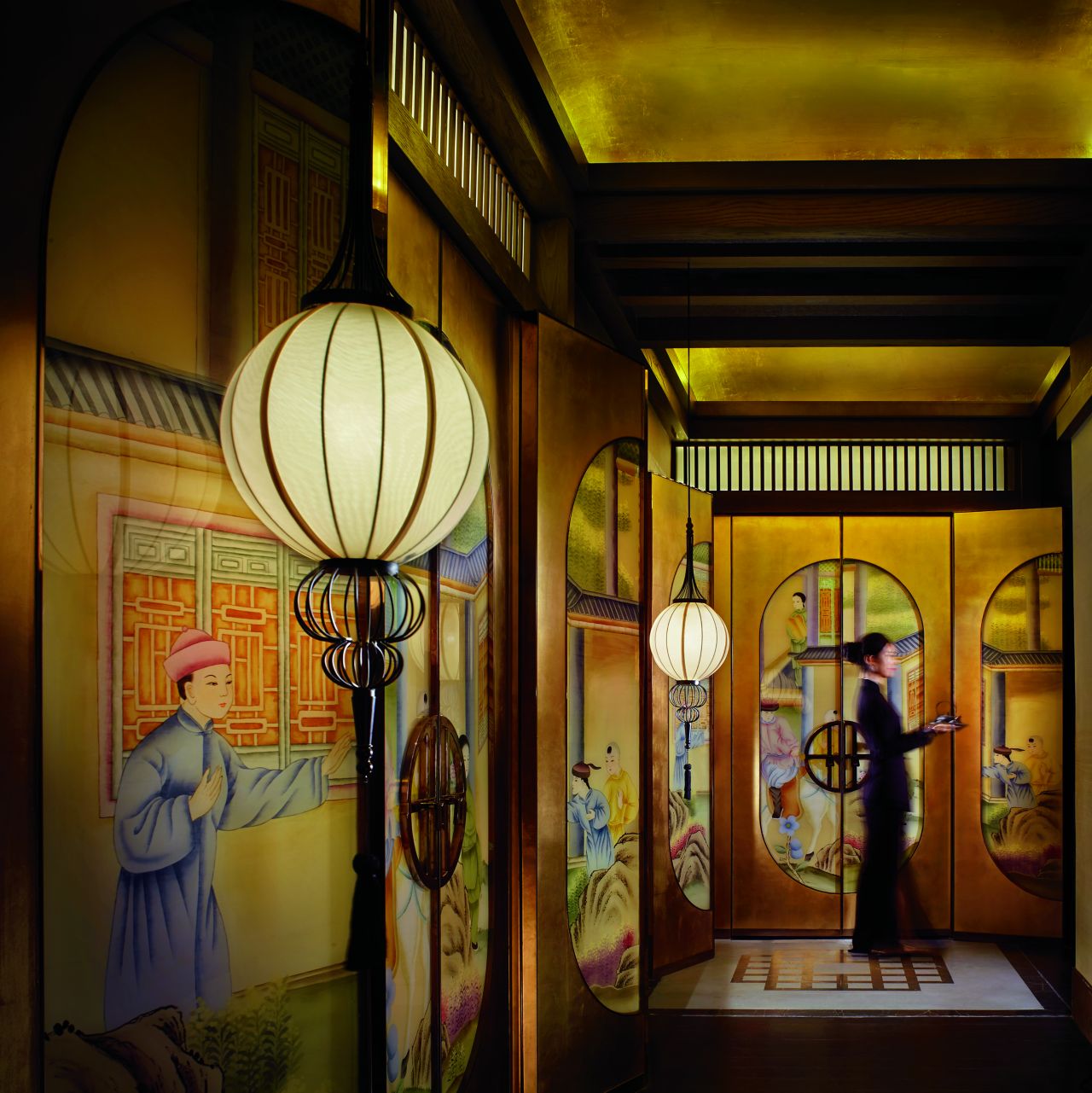 Waitress in a long dress in a hallway painted with traditional Chinese scenes