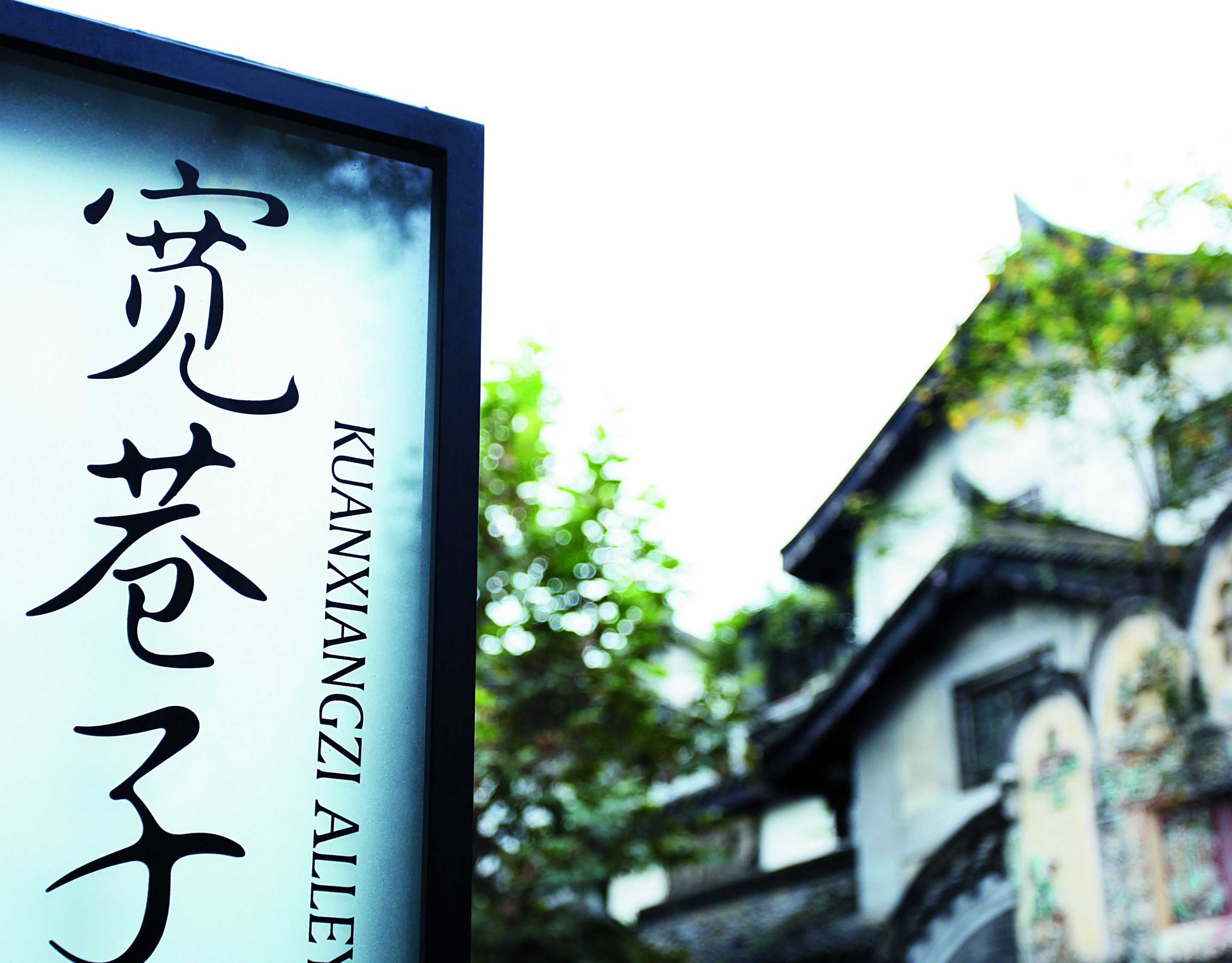 Sign that reads ?Kuan Zhai Alley? with a house and trees in the background