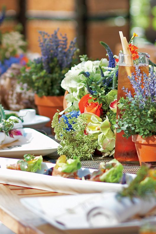 Table set with multiple flower pots and food decorated with flowers and greens