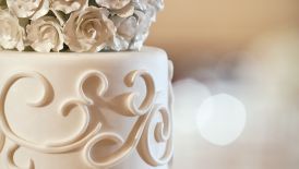 Close-up of the top tier of a wedding cake featuring a topper of white roses executed in frosting