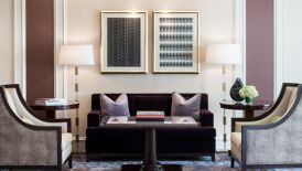 An elegant seating area with two armchairs and a sofa, a chandelier and framed artwork on the wall