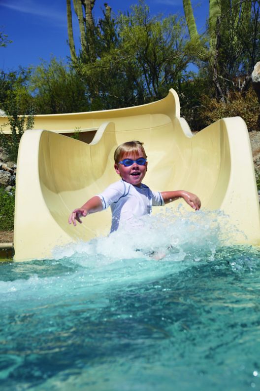 A little boy with goggles on going down a water slide.