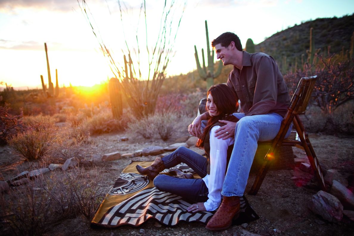 A man and woman sitting in the desert at sunset