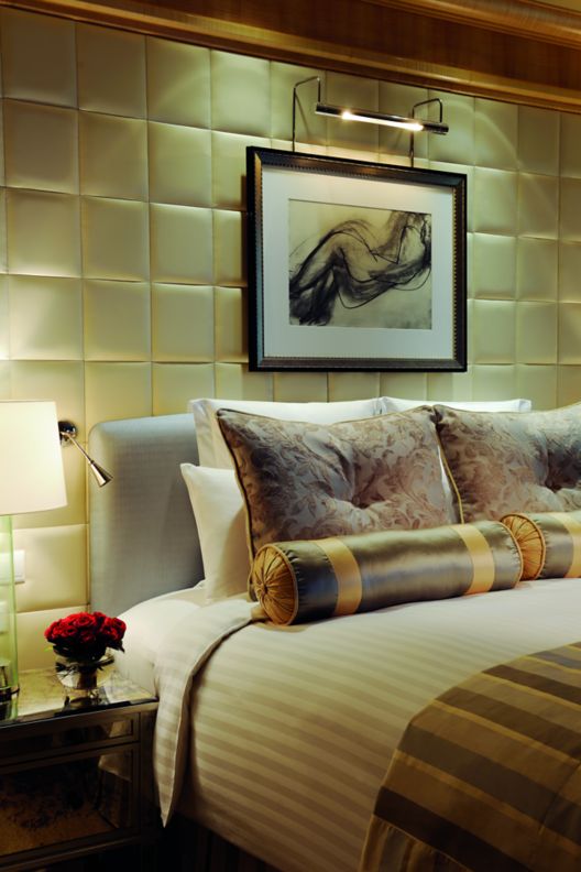 Hotel room bed with decorative pillows, art on the wall and a vase with flowers.