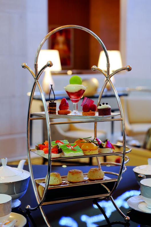 Three-tiered tray with scones and pastries flanked by tea cups and serving pieces