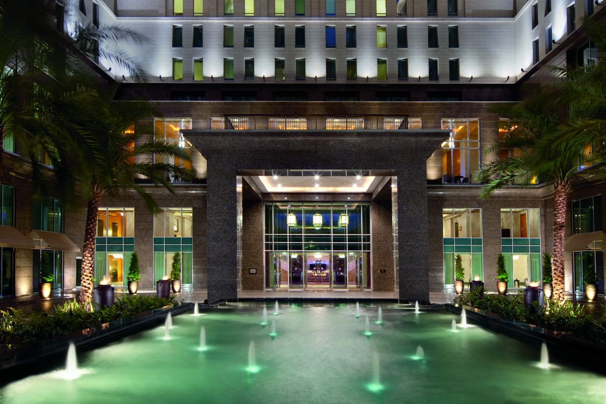 Hotel courtyard featuring an illuminated pool with fountains in the evening