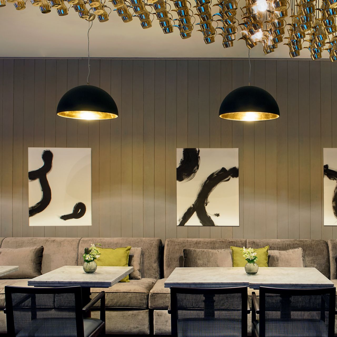 Modern restaurant seating with gray benches, white-and-black canvases and contemporary metal light fixtures