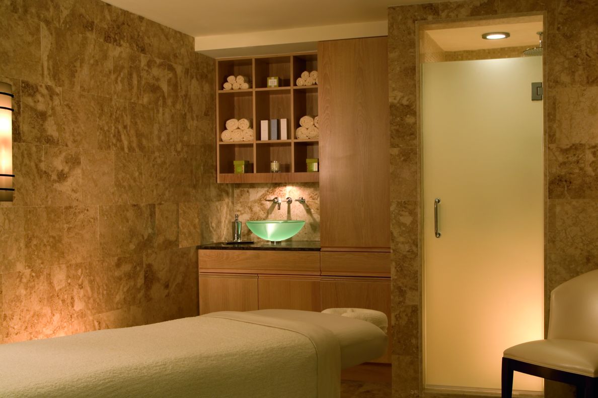 Room with a massage table, chair and a bowl sink with shelves above it