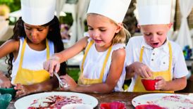 Two girls and a boy in aprons and toques prepare a berry dish