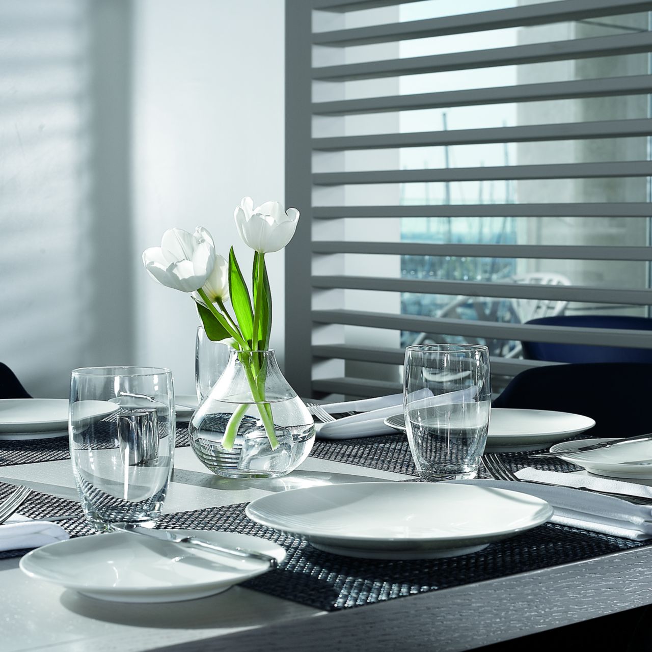 Table for four in shades of white and gray next to a white wall of slats