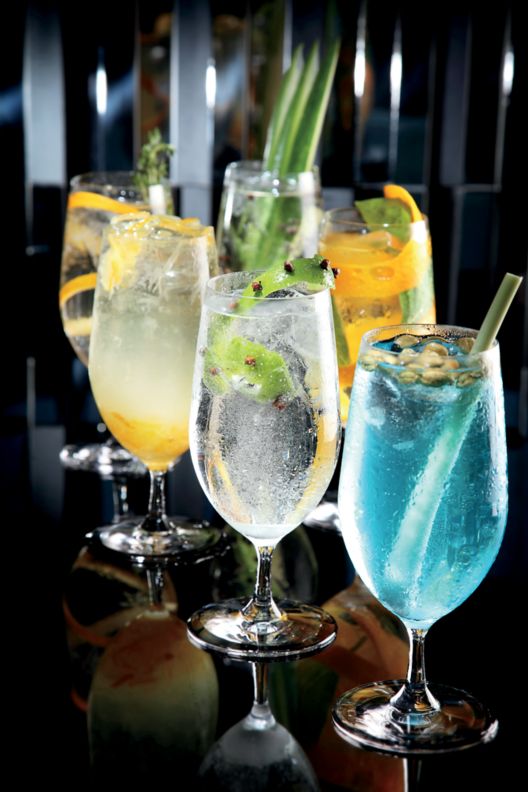 Specialty drinks in clear goblets with clear, yellow, and blue concoctions. 
