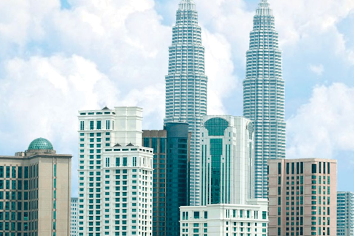 Kuala Lumpur skyline by day showcasing the Petronas Towers and other buildings as well as fluffy clouds and foliage