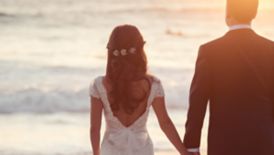 A bride and groom hold hands overlooking the ocean