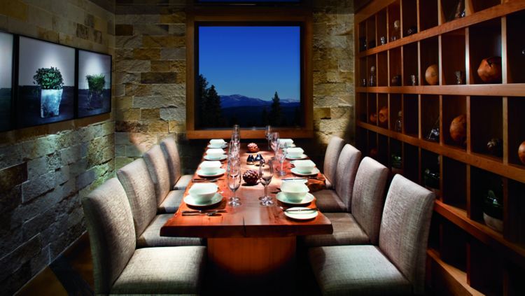 Intimate dining space with stone walls, a long wooden dining table and gray upholstered chairs