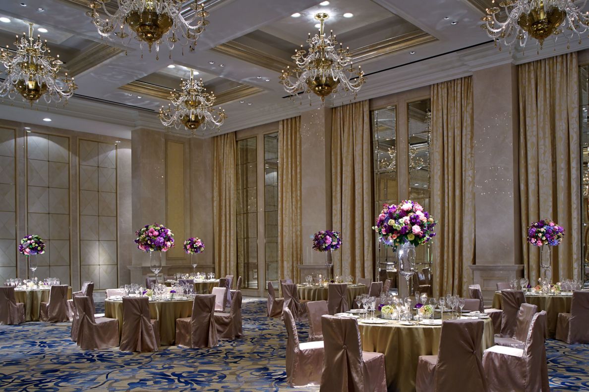 Large venue with patterned carpet, multiple chandeliers and round tables set for a formal meal