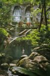 Streams of sunshine pierce dense foliage at an ancient temple comprised of stone carvings, massive boulders and a stream