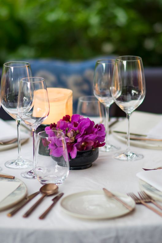 Outdoor roundtable with a white tablecloth, a small vase of exotic purple flowers and a candle