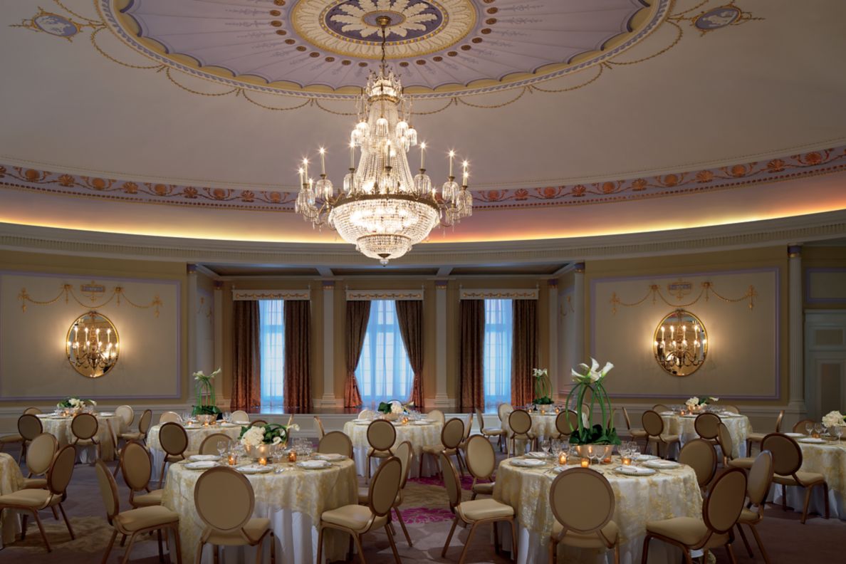 Banquet tables arranged in a round room with an ornate chandelier hanging in the center.