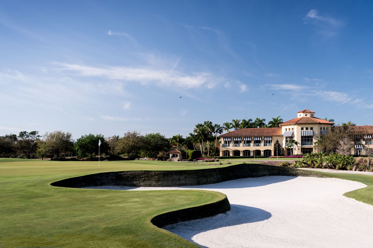 A golf course green with nearby, deep sand trap and the hotel's exterior in the background.
