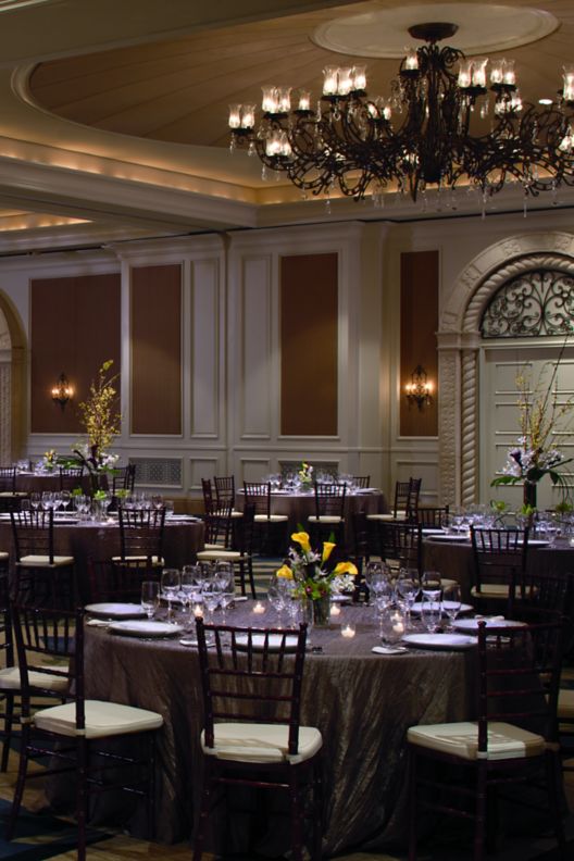 A room with large chandeliers, arched wall accents and multiple round dining tables