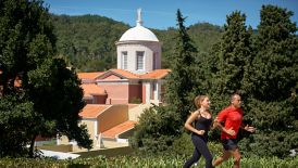 A man and woman run along a path overlooked by a traditional building with a domed tower