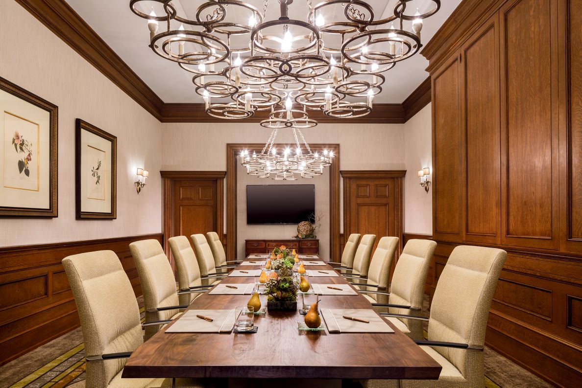 Board room with modern chandeliers, a wooden table with 10 chairs and a TV for presentations.