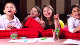 Four kids relax on red cushions with paper, crayons, treats and smiles