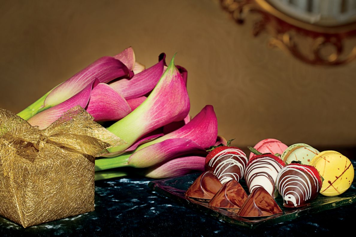 Bouquet of flowers laying on side table with a plate of chocolate covered strawberries. 
