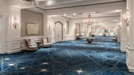 A wide carpeted hallway with chandeliers and seating areas