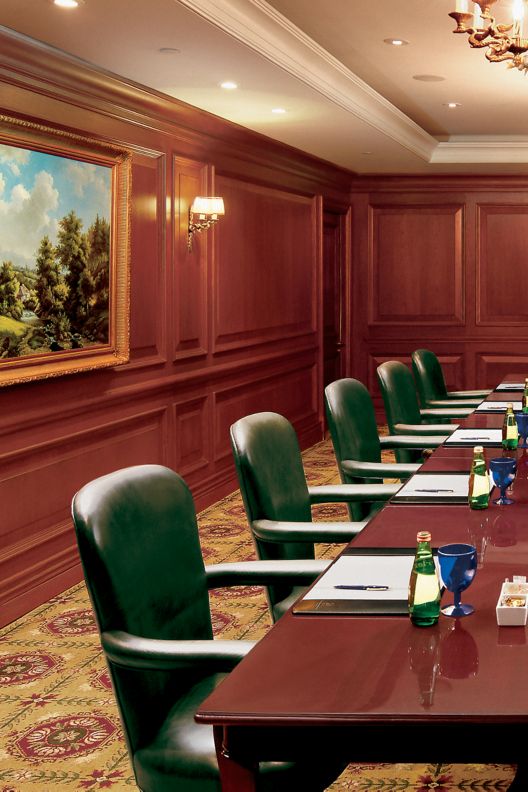 Conference desk with green executive chairs and wood paneling around the room. 